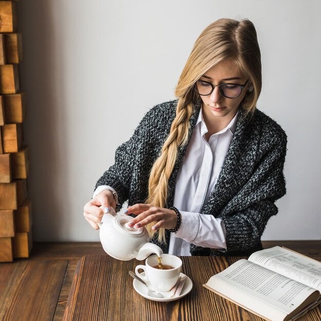 Taza de relleno linda mujer con té cerca de libro