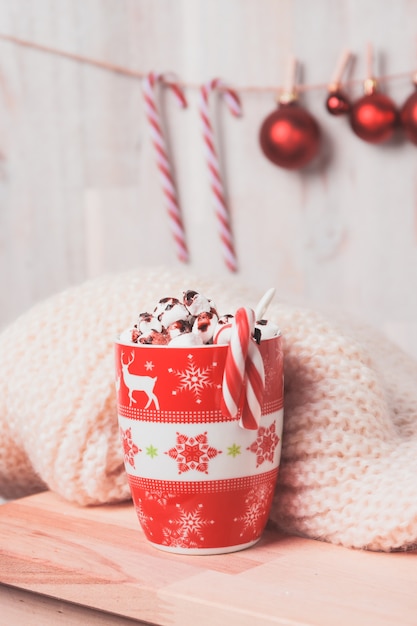 Taza roja con malvaviscos y bastones de caramelo y bolas de navidad