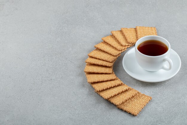 Una taza de té aromático con galletas saladas sobre un fondo gris.