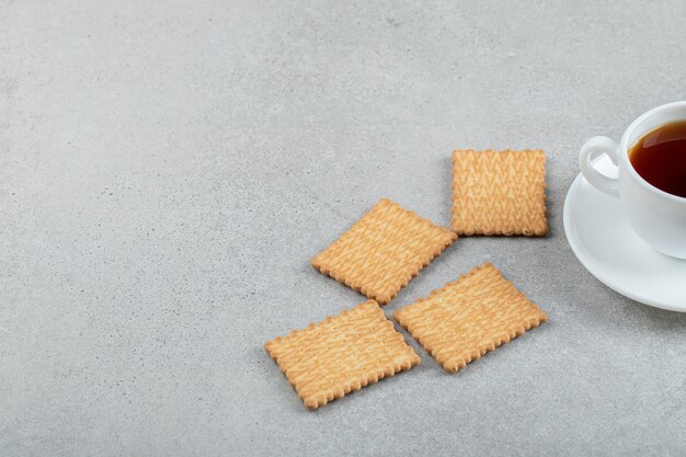 Taza de té aromático con sabrosas galletas saladas sobre una superficie de mármol.