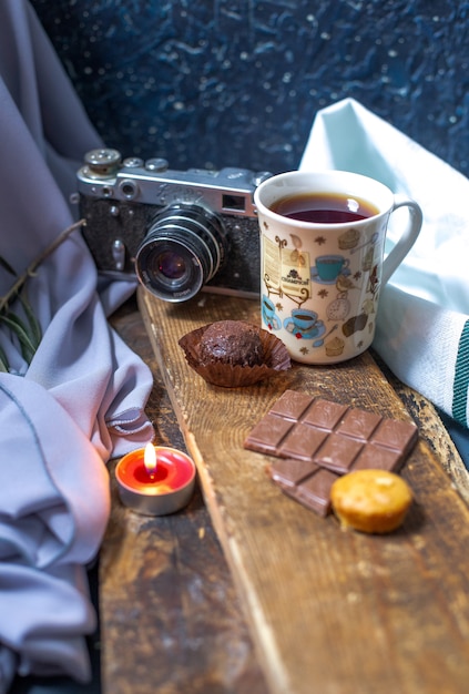 Foto gratuita una taza de té con barra de chocolate y magdalenas en un trozo de madera.