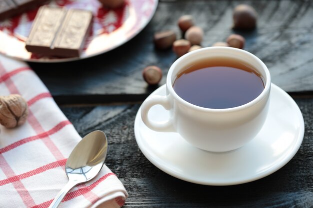 Una taza de té blanco con barra de chocolate y nueces alrededor.