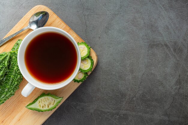 Una taza de té de calabaza amarga caliente con calabaza amarga cruda en rodajas coloque sobre una tabla de cortar de madera