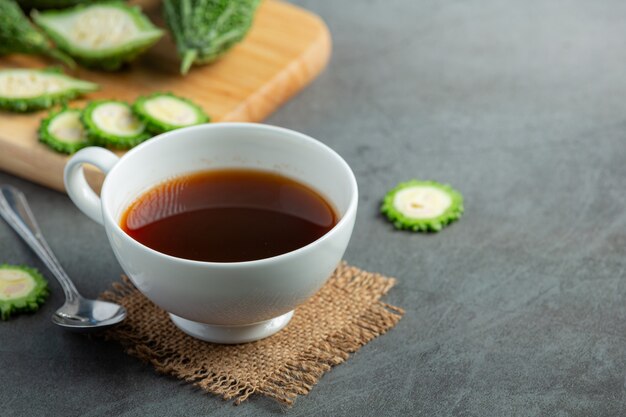 Una taza de té de calabaza amarga caliente con calabaza amarga cruda en rodajas lugar en el piso oscuro