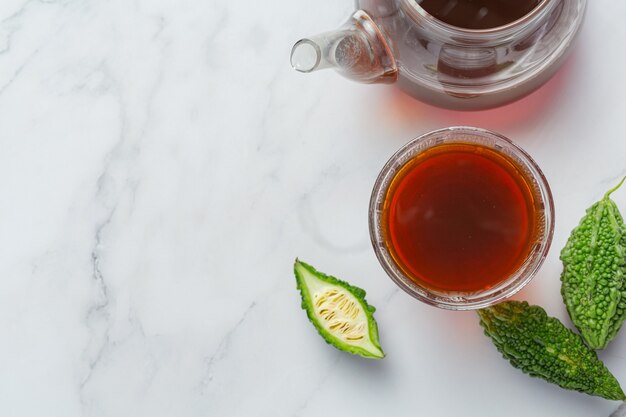 Una taza de té de calabaza amarga caliente con calabaza amarga en rodajas crudas sobre un piso de mármol blanco