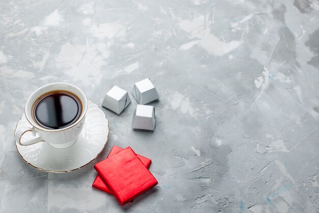 Taza de té caliente dentro de la taza blanca sobre placa de vidrio con paquete plateado, caramelos de chocolate en la mesa de luz, bebida de té, galleta de chocolate dulce, hora del té