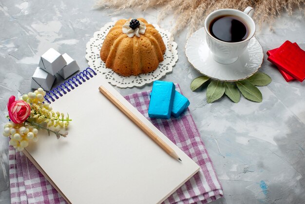 Taza de té caliente dentro de la taza blanca con tarta, bloc de notas, chocolates en la mesa de luz, té dulce de chocolate dulce