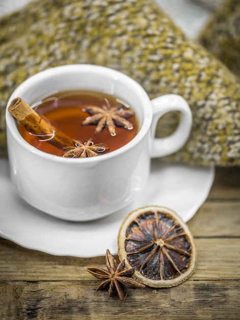 Una taza de té caliente con palitos de canela, especias y delicioso limón seco sobre madera con un suéter caliente