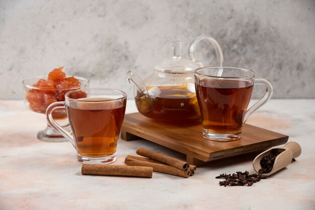 Taza de té caliente, tetera y mermelada de membrillo dulce sobre tabla de madera.
