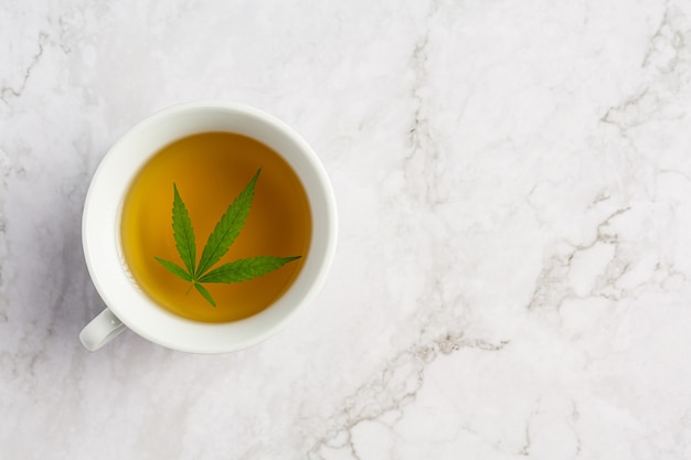 Taza de té de cáñamo con hojas de cáñamo en suelo de mármol blanco