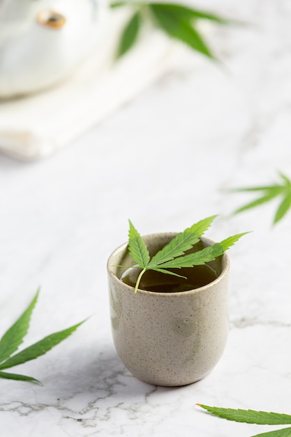 Taza de té de cáñamo con hojas de cáñamo en suelo de mármol blanco