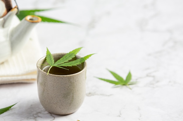 Taza de té de cáñamo con hojas de cáñamo en suelo de mármol blanco