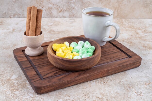 Taza de té, canela y dulces en tablero de madera