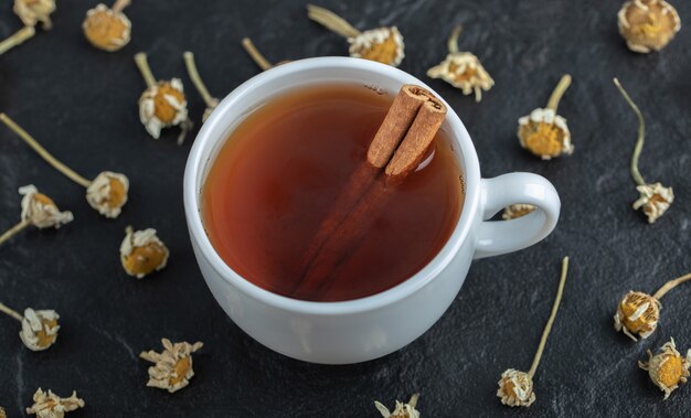 Taza de té con canela y montón de manzanillas secas.