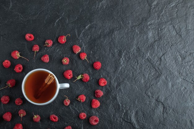 Taza de té con canela en rama y frambuesas maduras.