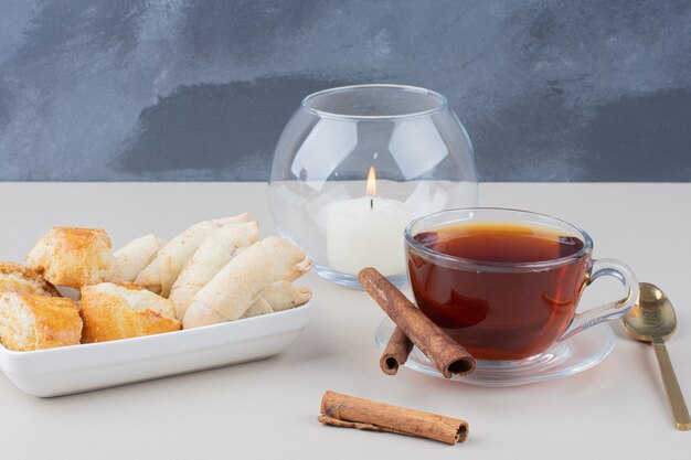 Una taza de té con canela y varias galletas sobre la superficie blanca.