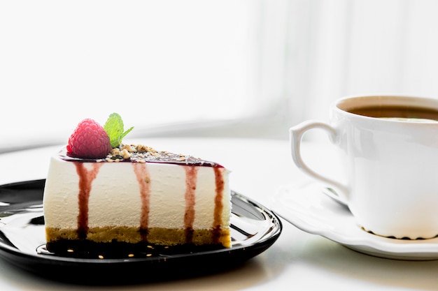 Taza de té cerca del pastel de queso casero con bayas frescas y menta para el postre en la mesa