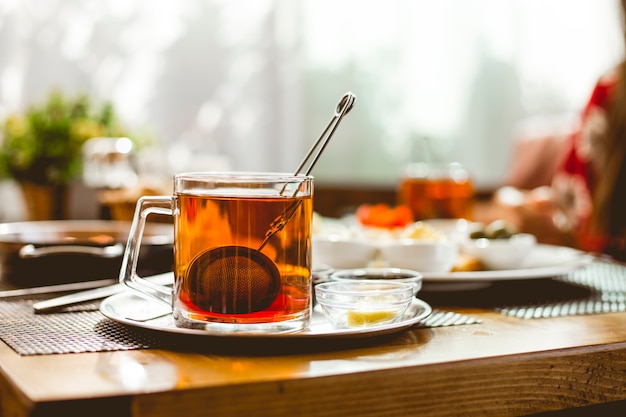 Taza de té con colador de té dentro de mermelada de limón en la vista lateral del platillo