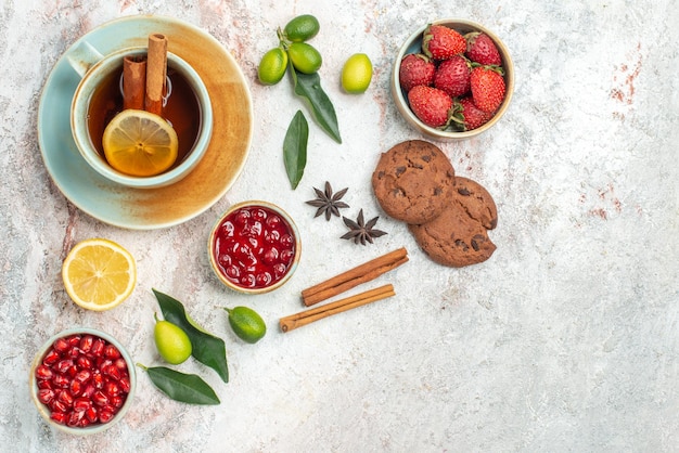 una taza de té cuencos de bayas cítricos anís estrellado y palitos de canela galletas de chocolate junto a la taza de té con canela en la mesa