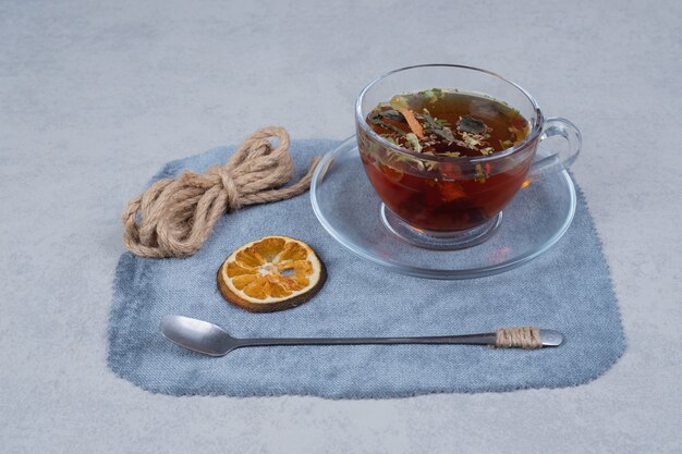 Taza de té, cuerda y rodaja de naranja seca sobre mantel.