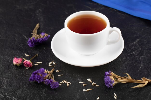 Una taza de té con flores secas sobre una mesa negra.