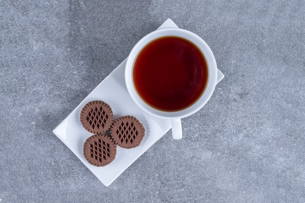 Taza de té y galletas de cacao en la placa blanca.