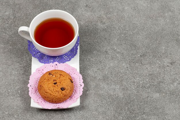 Taza de té y galletas de chispas en platillo blanco