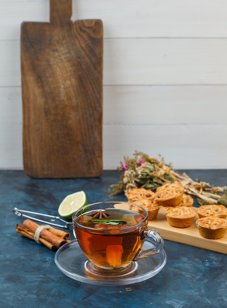 Taza de té y galletas con galletas, flores, canela, limón y colador de té