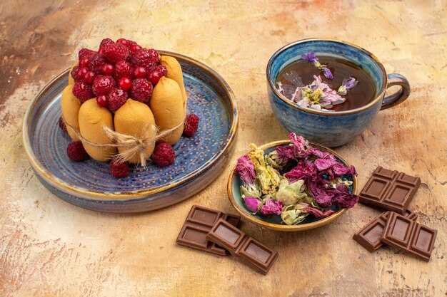 Una taza de té de hierbas caliente pastel suave con frutas, flores, barras de chocolate en la tabla de colores mezclados