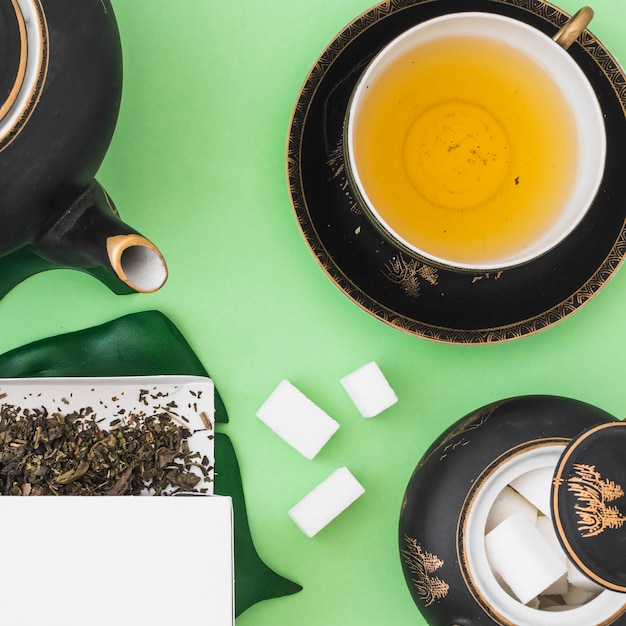 Taza de té de hierbas con cubos de azúcar sobre fondo verde