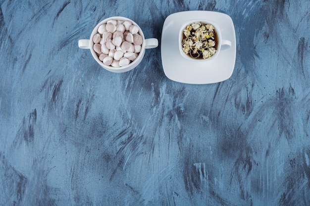 Taza de té de hierbas con cuenco de caramelos marrones sobre fondo azul.