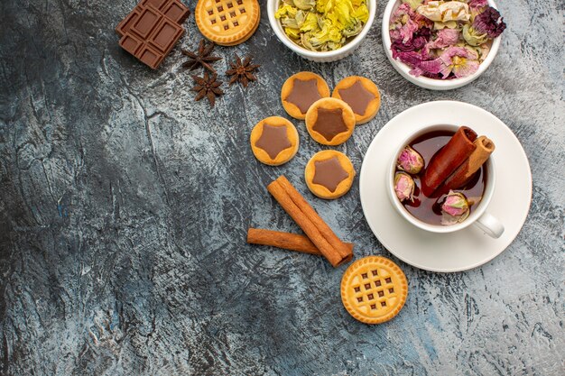 Una taza de té de hierbas con cuencos de flores secas y galletas y canela en gris