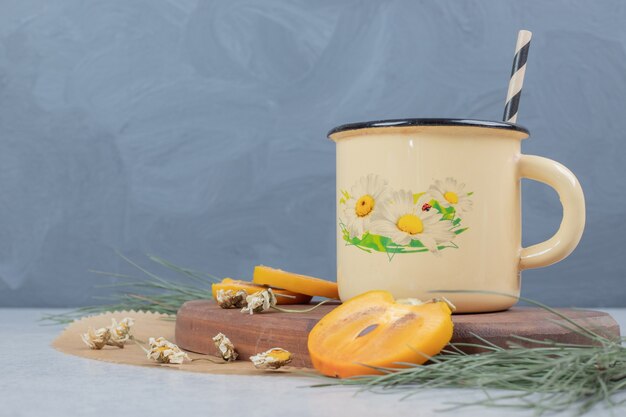 Taza de té de hierbas, flores y rodajas de caqui sobre tabla de madera. Foto de alta calidad