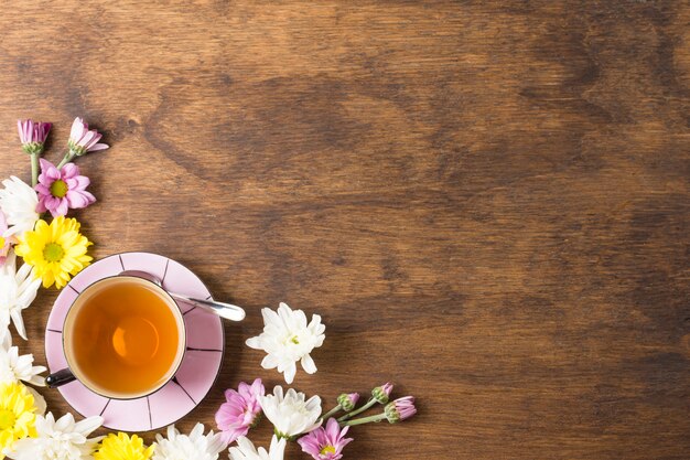 Taza de té de hierbas y hermosas flores en la esquina del fondo de madera