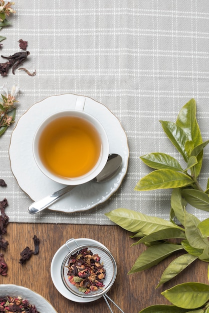 Taza de té de hierbas; Hierbas secas y hojas en mantel sobre la mesa.