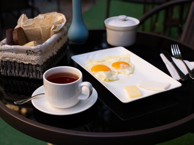 Una taza de té y huevos fritos sobre la mesa negra.