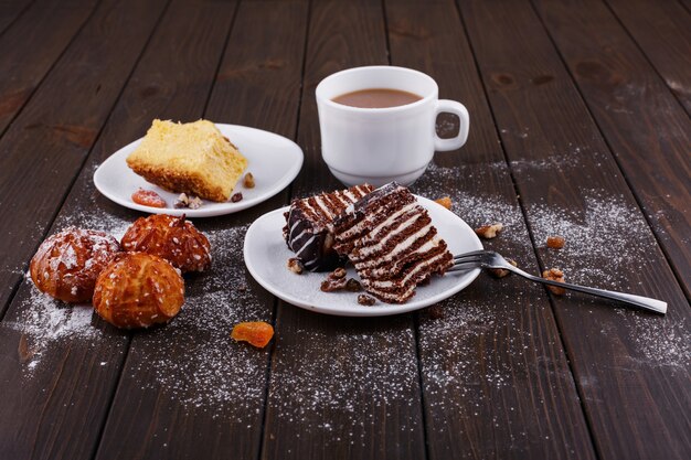 Taza de té con leche y dos platos con tarta de queso y chocolate