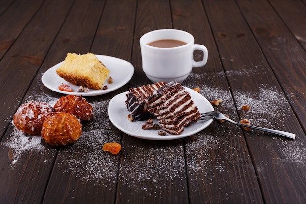 Taza de té con leche y dos platos con tarta de queso y chocolate