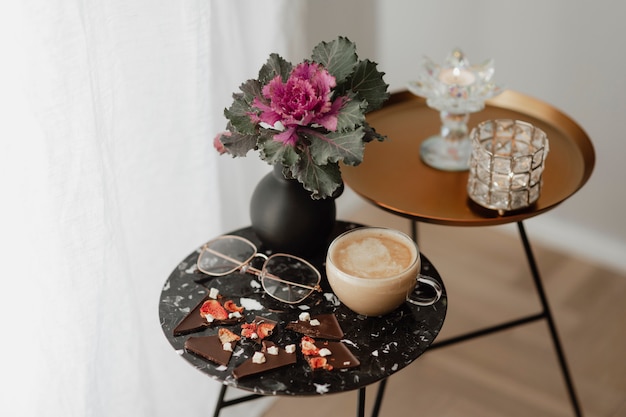 Taza de té con leche y lentes en una mesa negra al lado de una cortina