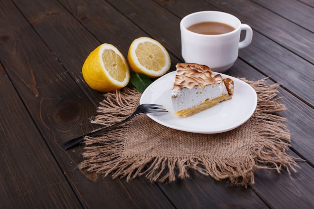 La taza de té con leche y el pedazo de pue del limón sirvieron en la tabla de madera oscura