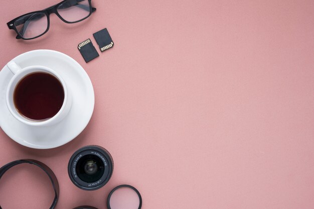 Taza de té; lente de la cámara; espectáculo; Tarjetas de memoria y anillos de extensión sobre color rosa.