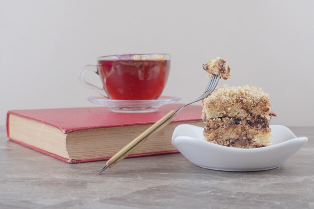 Una taza de té en un libro junto a una pequeña porción de pastel de mármol