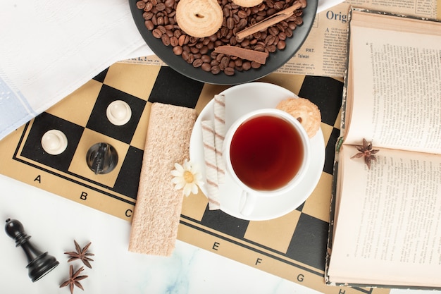 Una taza de té y un libro en un tablero de ajedrez.