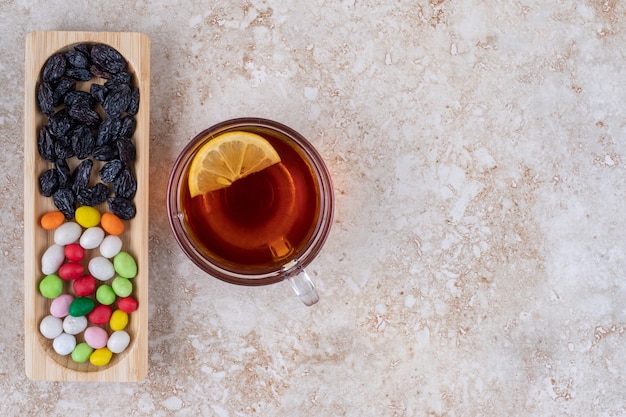 Taza de té con limón y plato de dulces en superficie de mármol