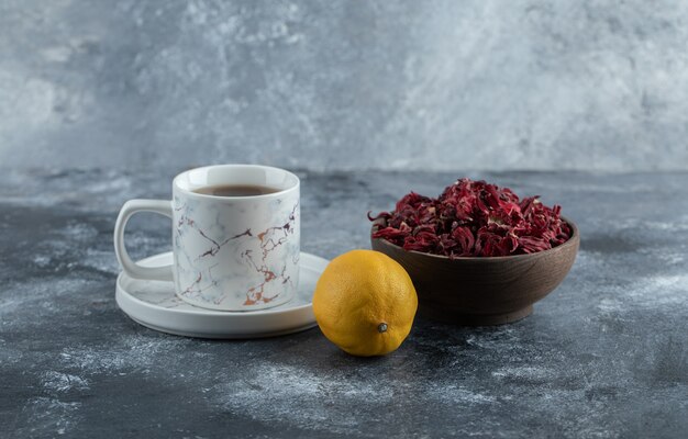 Taza de té, limón y tazón de flores secas en la mesa de mármol.