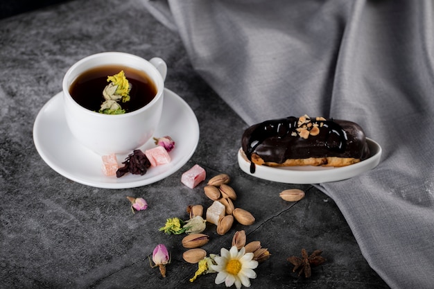 Una taza de té con lokum turco, pistachos y eclair de chocolate.