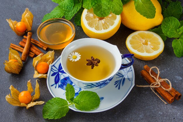 Una taza de té de manzanilla con hojas de menta, limón, miel, canela seca, vista de ángulo alto