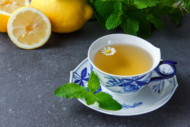 Una taza de té de manzanilla con hojas de menta, limón, vista de ángulo alto.