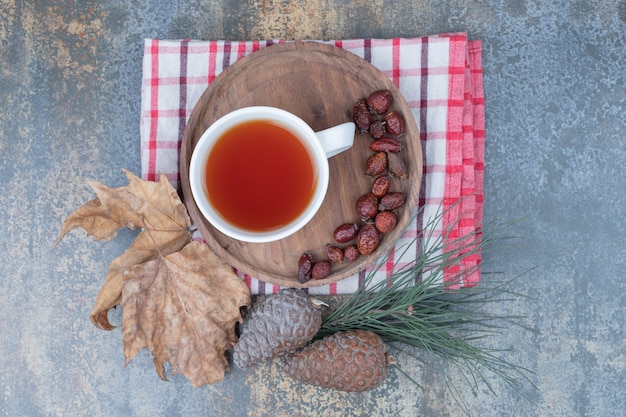 Taza de té negro y escaramujos secos en placa de madera con piñas. Foto de alta calidad