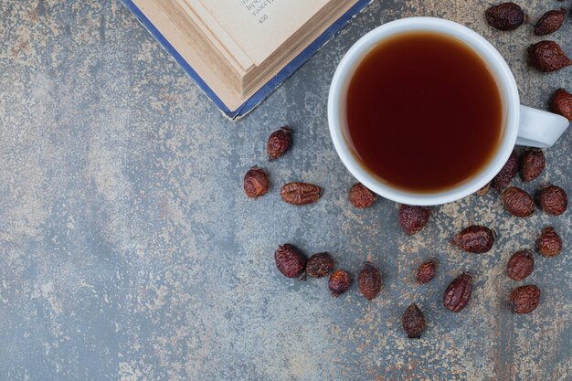 Taza de té negro y rosa mosqueta seca sobre fondo de mármol. Foto de alta calidad